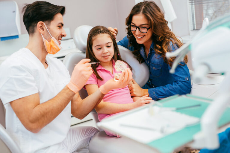 child sitting in dental chair with parent next to chair