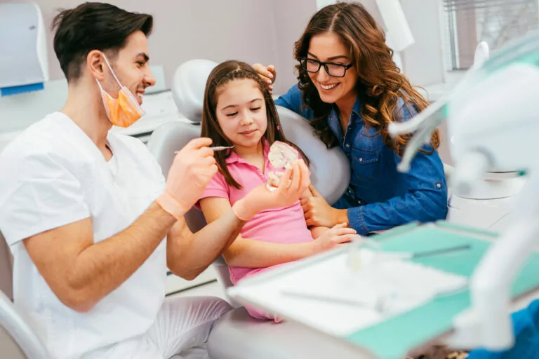child sitting in dental chair with parent next to chair