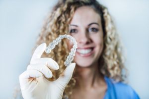 Photo of a female doctor, focused on her hand that is holding a transparent dental aligner