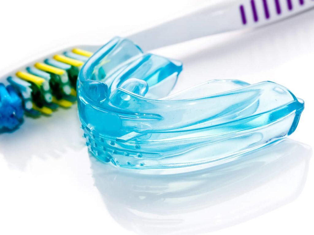 A blue transparent mouth guard sits next to a toothbrush