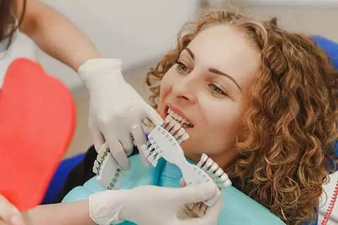 woman in dental chair comparing different shades of teeth
